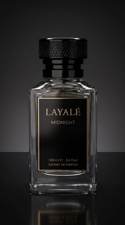 A clear glass perfume bottle with a black textured cap and a black front label featuring gold lettering that reads 'LAYALÉ MIDNIGHT'. The bottle is centered against a dark gray gradient background with a reflective black surface below.