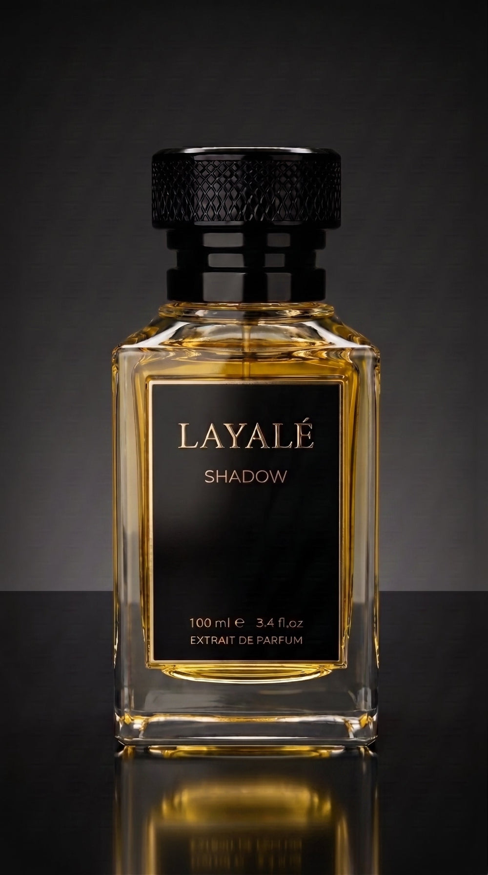 A rectangular glass perfume bottle filled with amber liquid, featuring a black cap and a black front label with gold lettering that reads 'LAYALÉ SHADOW'. The bottle is centered against a dark gray gradient background with a reflective surface below.